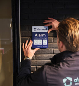 Een medewerker bevestigt het waarschuwingsbord van Alarmed op de gevel van een pand.